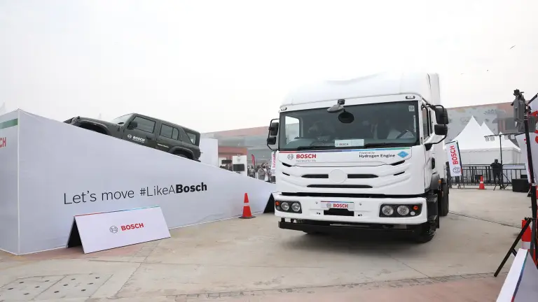 Ein weißer Lkw fährt einen Parcours entlang, während ein Jeep auf eine Rampe fährt.