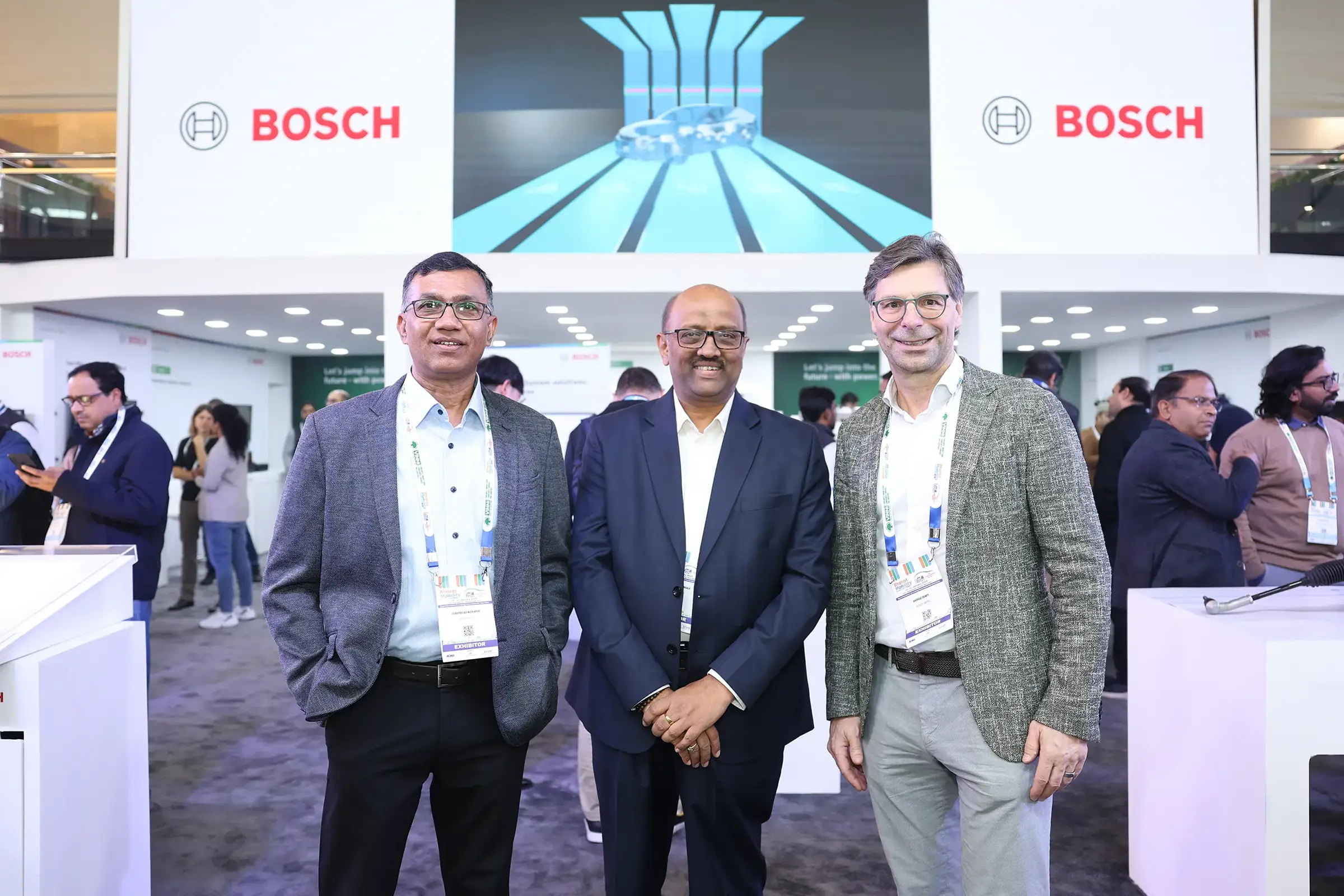 Three men in business attire stand at the Bosch booth at BMGE
