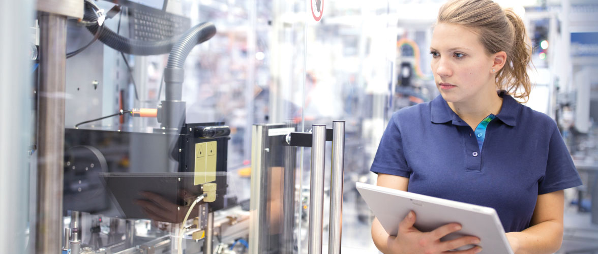 A woman with a tablet examines a machine during production.