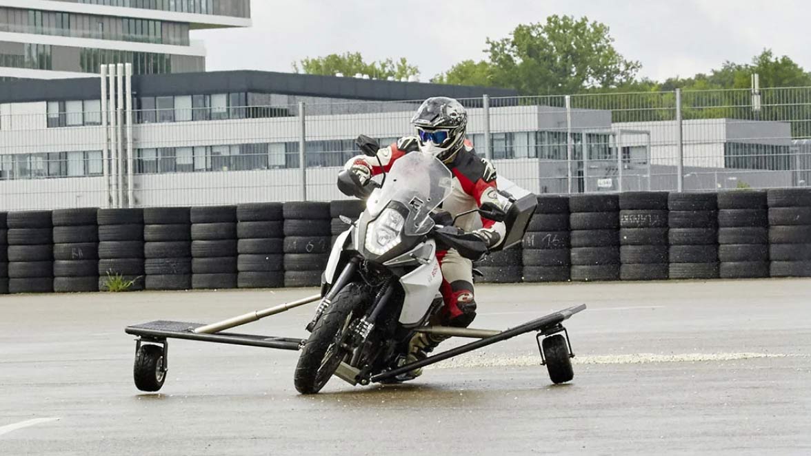 Front view of a motorcycle rider on a test track with wheel supports
